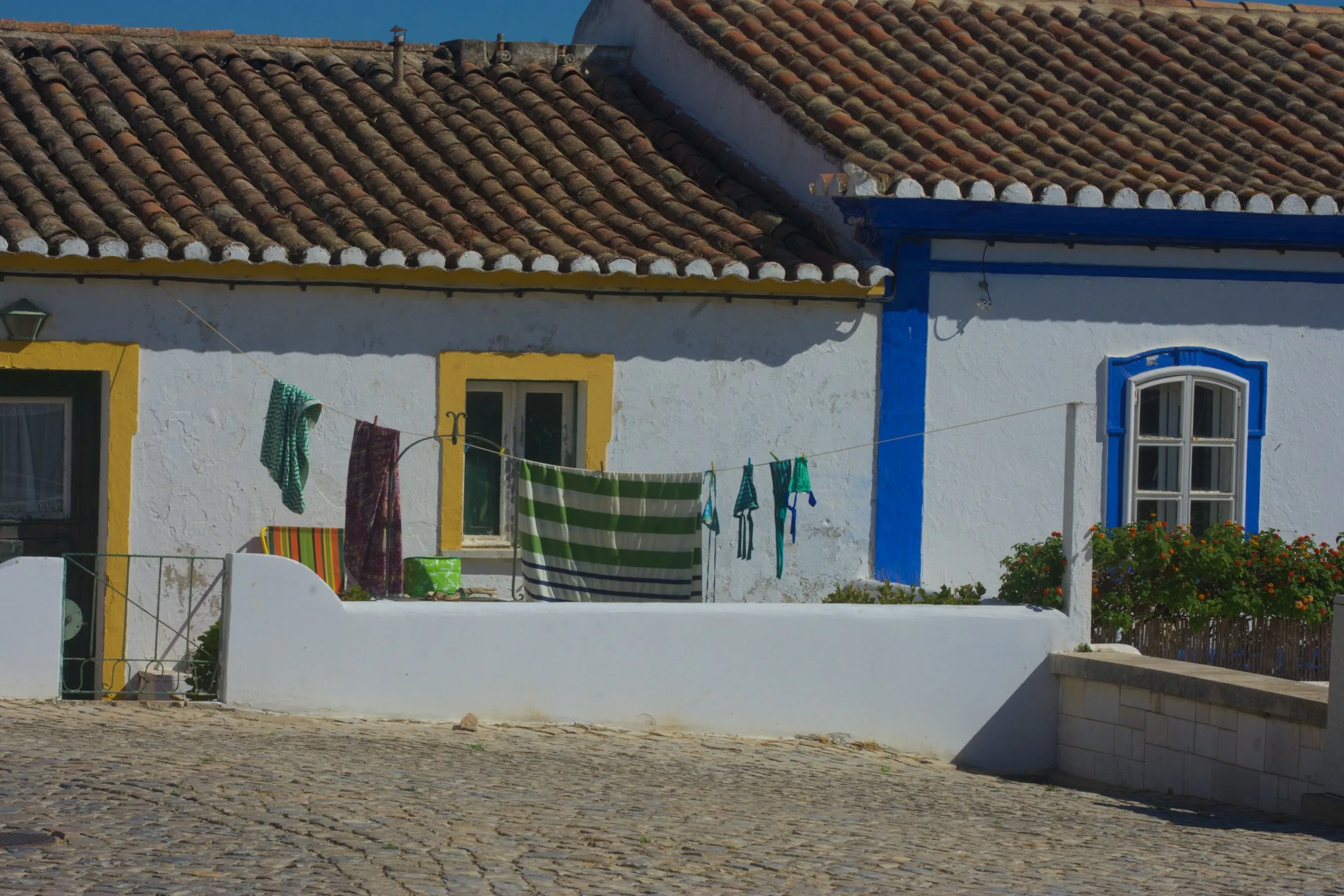 Casa caiada de branco com barras azuis e amarelas numa rua de calçada